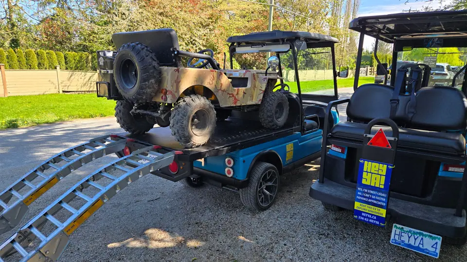A HeyYa electric flatdeck carrying a small off-road vehicle, with loading ramps lowered