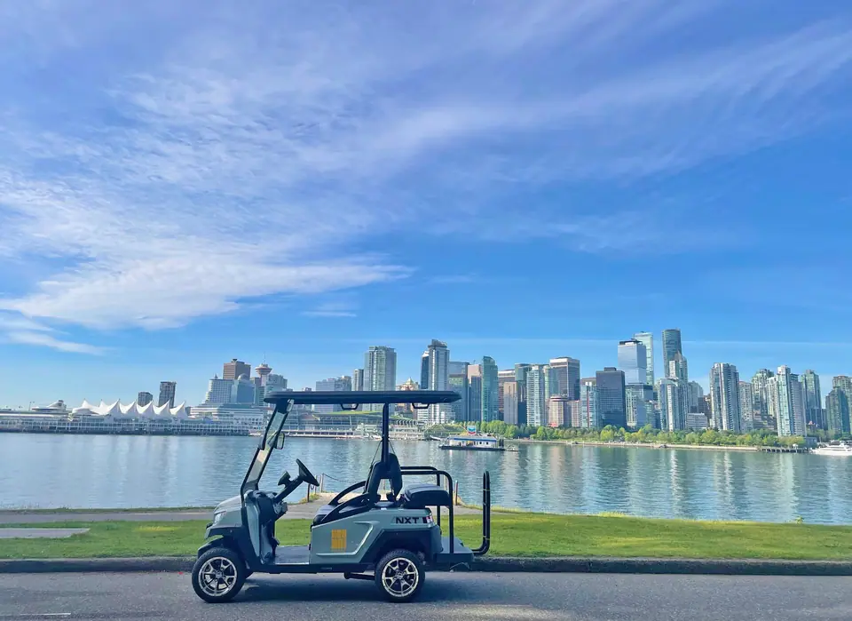 A HeyYa cart parked on a Stanley Park road with the downtown Vancouver skyline across the harbour